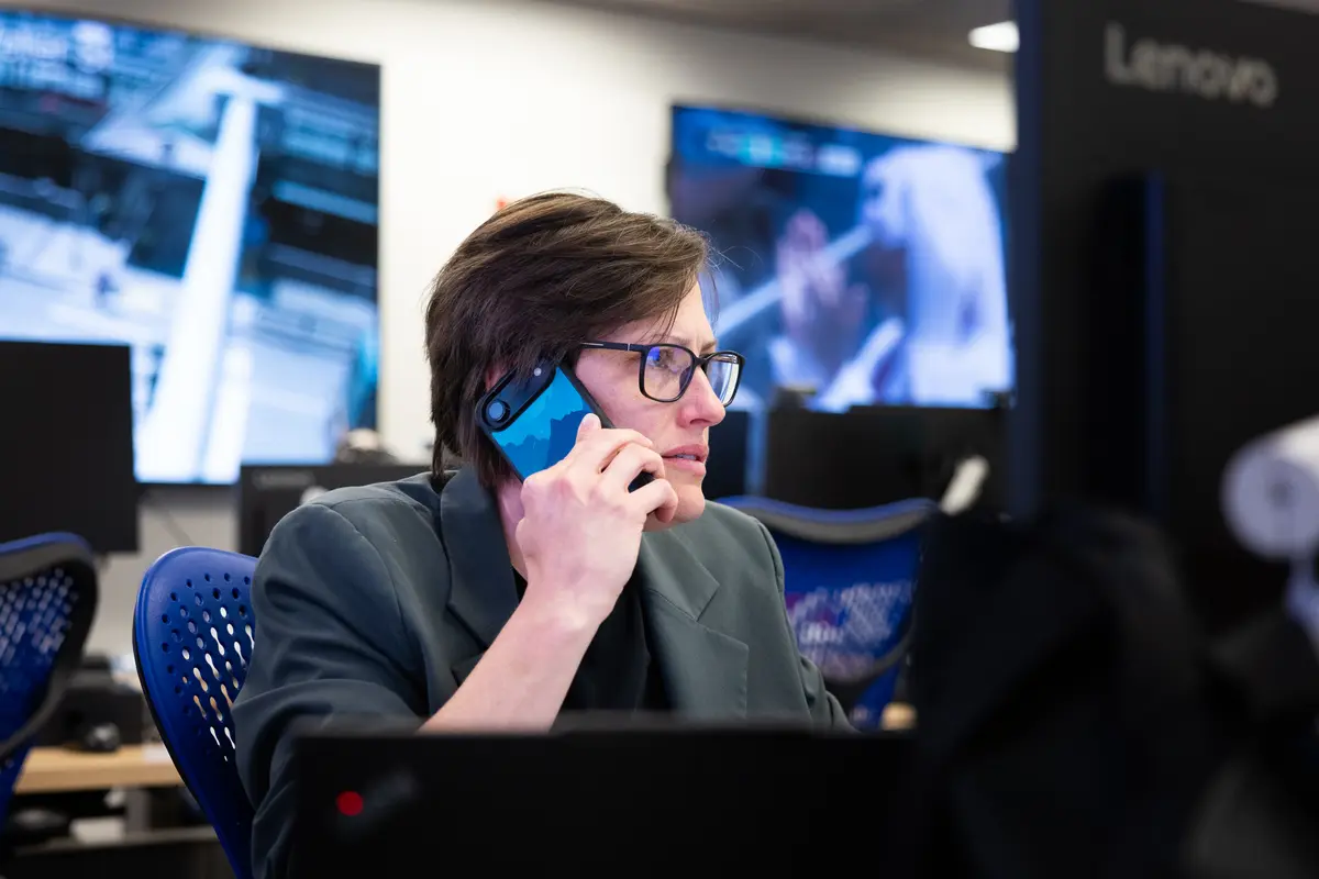 A staff member on the phone in the Emergency Operations Center, with security monitors visible behind her