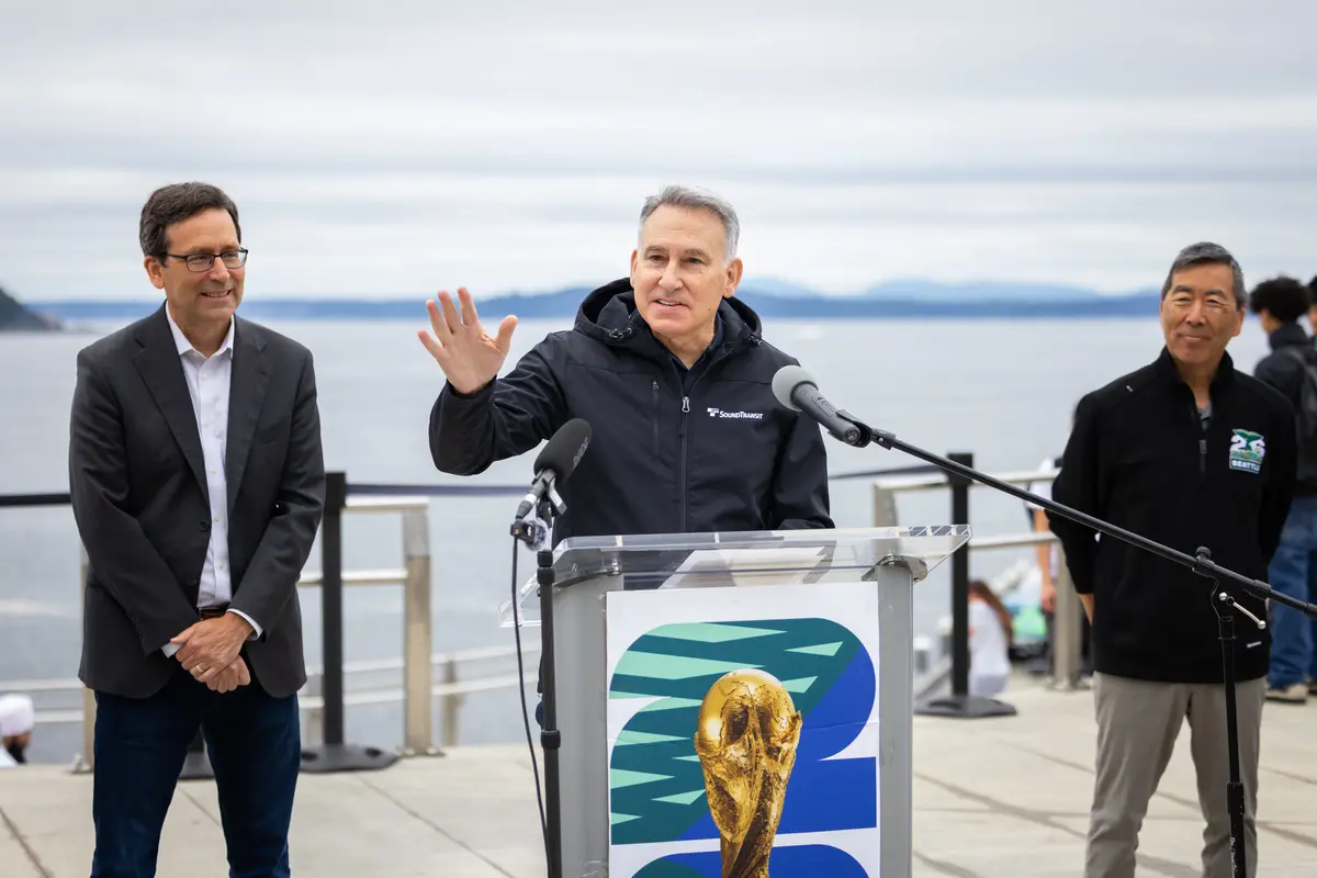 Governor Bob Ferguson watches Sound Transit CEO Dow Constantine speak at a podium bearing a World Cup trophy graphic